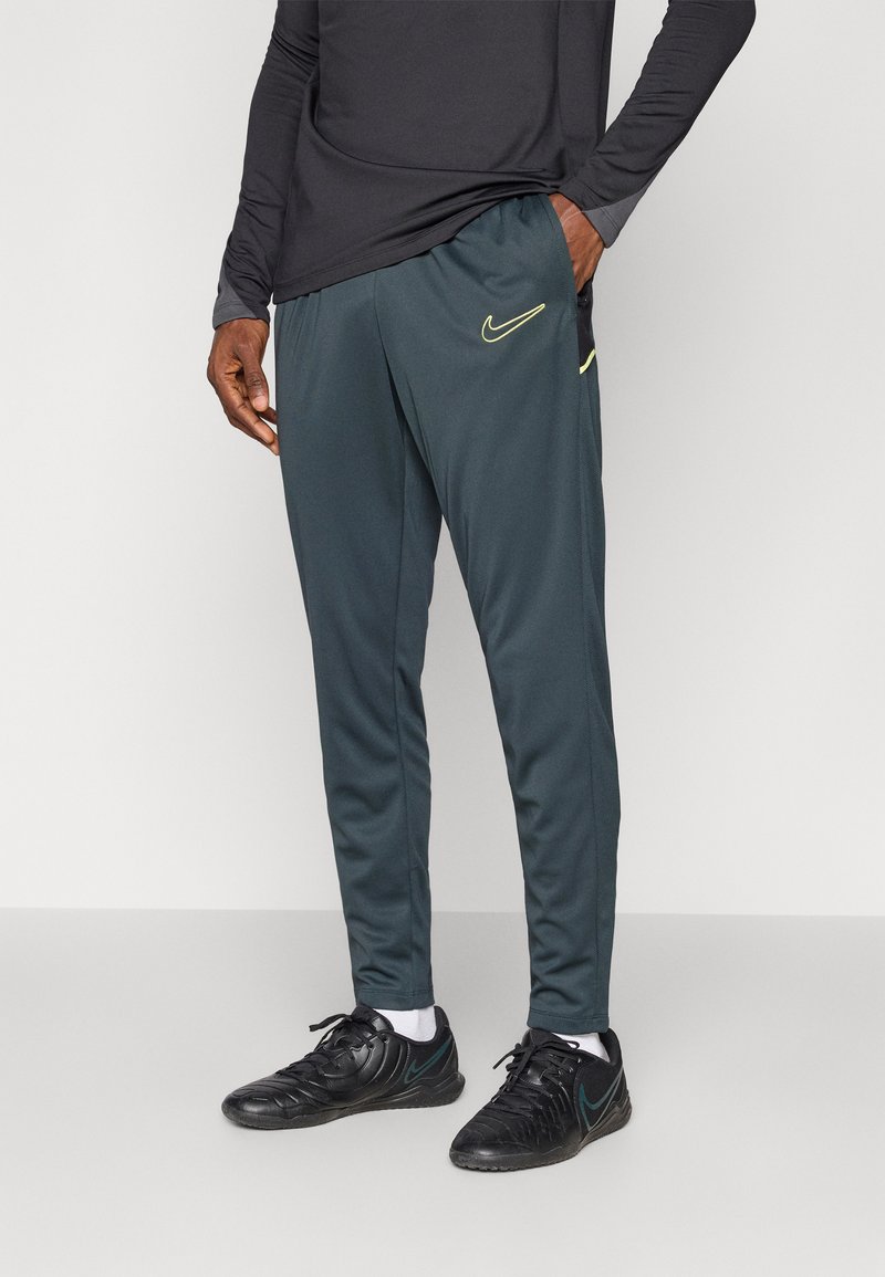 Męskie ciemnozielone spodnie sportowe wykonane z lekkiego materiału, z elastycznym pasem oraz neonowo-żółtym logo Nike z przodu.