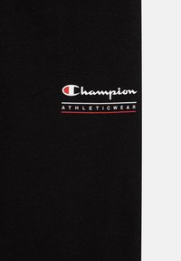 Juodas medvilnės audinys su logotipu, kuriame baltais rašmenimis parašyta „Champion“, o raudonais – „ATHLETICWEAR“. Paprastas, švarus dizainas be papildomų raštų.