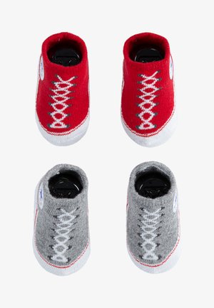 Calzini per neonati in maglia rossi e grigi che assomigliano a sneakers, con suole bianche e disegni di lacci. Presentano un patch rotondo con logo su ciascun lato.