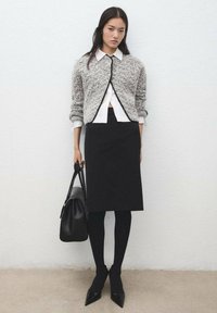 Sivi teksturirani kardigan s crnim rubom, bijela košulja s ovratnikom, crna uska suknja, crne hulahopke, cipele sa šiljatim vrhom i crna torba.