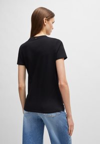 T-shirt en coton noir à manches courtes et col rond, avec un petit accent orange près de l'encolure, associé à un jean bleu clair.