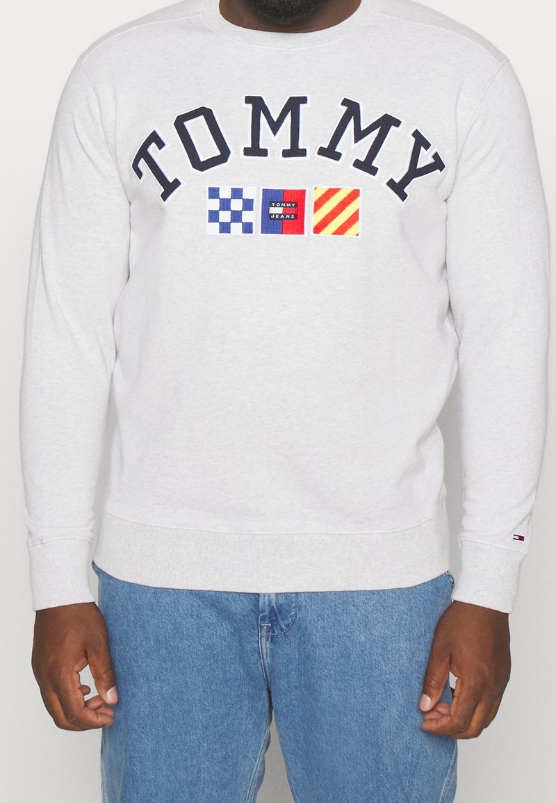 Felpa grigia con polsini e orlo a costine, con la scritta “TOMMY” in blu scuro e quadrati logo ricamati in blu, rosso e giallo.