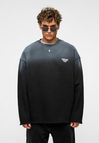 Zwarte gradient sweatshirt met lange mouwen, ronde hals en logodetail. Draag met donkere spijkerbroeken en gelaagde kettingen; zachte textuur.