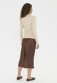Beige långärmad topp i kombination med en brun satinmidikjol. Släta texturer, avslappnad passform och platta bruna sandaler fulländar looken.