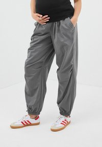 Pantalons gris, légers et élastiqués avec poches latérales et poignets froncés, associés à des baskets blanches et rouges avec semelles en gomme.