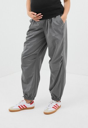 Graue, leichte, elastische Hosen mit Seitentaschen und gerafften Bündchen, kombiniert mit weißen und roten Turnschuhen mit Gummisohlen.