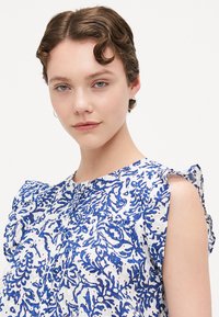 Floral design blouse in white and blue, made from lightweight fabric. Features ruffled sleeves and a buttoned front. Smooth texture.