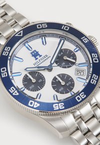 Silberner Edelstahl-Chronograph mit blauer Lünette, weißem Ziffernblatt, schwarzen Unterzifferblättern und erhöhten Stundenmarkierungen. Wasserfest.