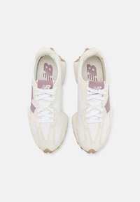 Paire de baskets blanches et beiges New Balance avec des accents violet clair et des lacets blancs, vues de dessus sur un fond clair.