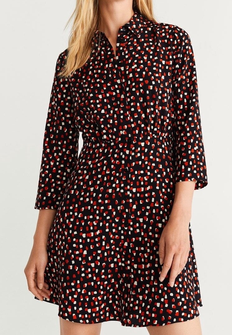 Femme portant une robe noire avec un motif abstrait de points rouges et blancs, manches trois-quarts et taille cintrée.