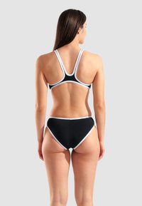 Juodas bikini maudymosi kostiumėlis su baltais akcentais, turintis sportinį dizainą, reguliuojamus dirželius ir aukštai kirptus šortus, užtikrinančius vengimo efektą.