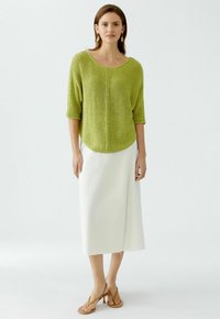 Green knitted top with a wide neckline and short sleeves, paired with a white mid-length skirt and tan heeled sandals. Plain background.