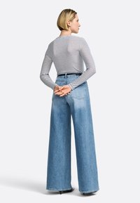 Gestreifes Langarmoberteil in Kombination mit weit geschnittenen, hellblauen Jeans. Das Outfit hat eine hohe Taille und eine lockere Passform mit schmal zulaufendem Saum.