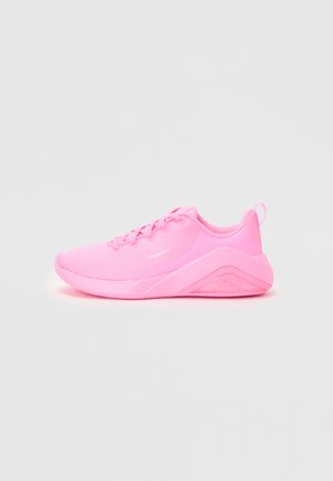 Pink athletic shoes with a mesh upper, round toe, and flat laces. The sole has a textured grip, featuring a logo on the side.