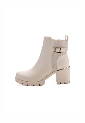 Beige ankle boot with a chunky heel, made of smooth and textured materials, featuring a gold buckle on the side and a pull tab on the back.