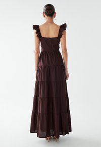 Lange bordeauxrode jurk met gelaagd ontwerp, ruchebandjes en een vierkante rug. Gemaakt van lichtgewicht stof en voorzien van een ritssluiting.
