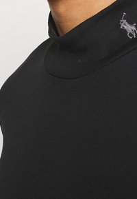 Svart polotröja i slät tyg med en åtsittande design; har en subtil logotyp på kragen.