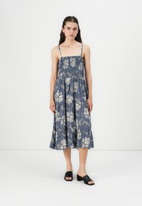 Blå blommig midiklänning med smockad bodice, tunna axelremmar och utsvängd kjol. Kombinerad med svarta öppna klackmules.