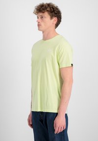 Hellgrünes Baumwoll-T-Shirt mit kurzen Ärmeln, Rundhalsausschnitt und einem kleinen weißen Logo auf der Brust. Kombiniert mit dunkelblauer Jeans.