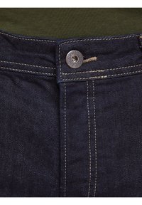 Mörkblå denimjeans med silverdetaljer, kontrastsömmar, metallknäppt stängning och en strukturerad tygtextur.