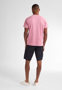 Rosa Kurzarm-T-Shirt mit Rundhalsausschnitt, kombiniert mit dunklen Cargo-Shorts und hellen Sneakern. Der Fokus liegt auf einer lockeren Passform und lässigem Stil.