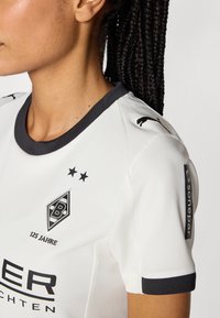 Bijela sportska majica s crnim ovratnikom i manžetama, s izvezenim logom, dva zvjezdice i imenom sponzora na rukavu.