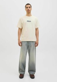 Cream short-sleeve T-shirt with blue "Originals Summer Edition" text, paired with light blue wide-leg jeans and brown shoes.