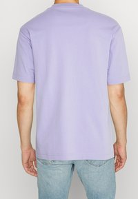T-shirt lilas à manches courtes en coton, avec un col rond et une coupe décontractée, associé à un jean en denim bleu clair.