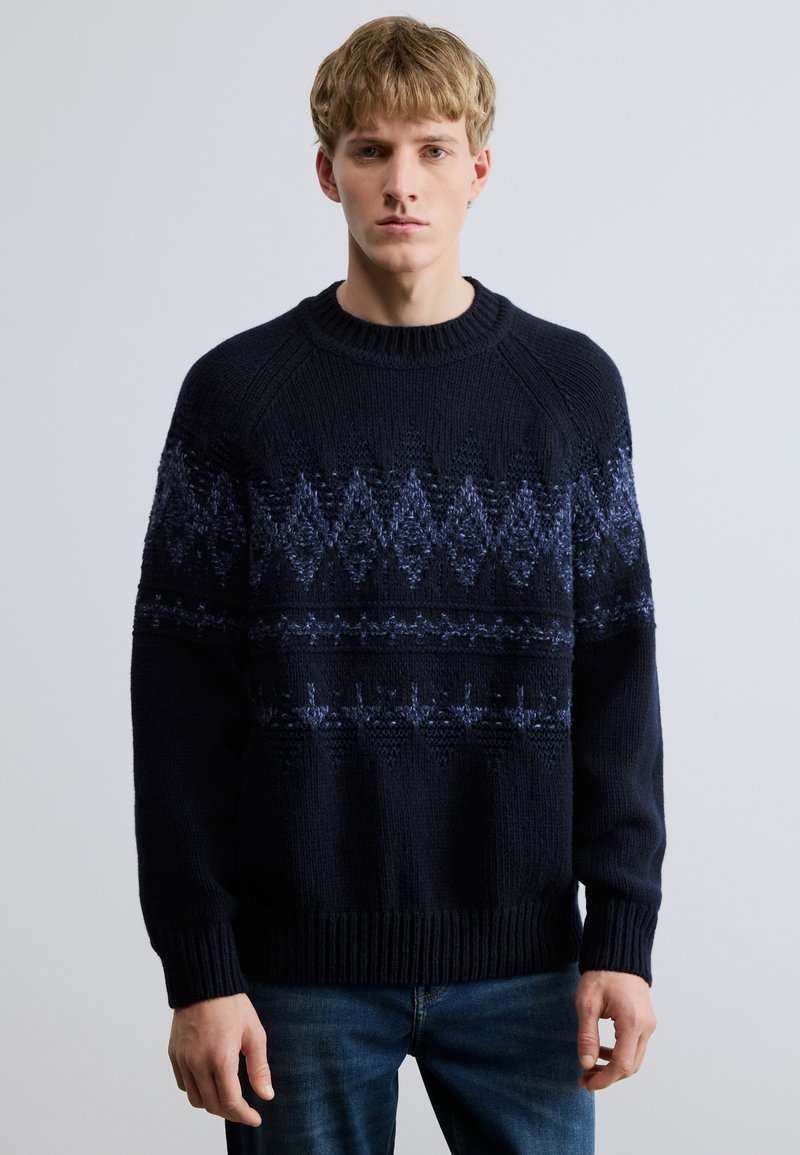 Tengerészkék kötött pulóver, texturált mintával, világosabb árnyalatú geometriai mintákkal, bordázott nyakkivágással és mandzsettákkal, valamint kényelmes szabással.