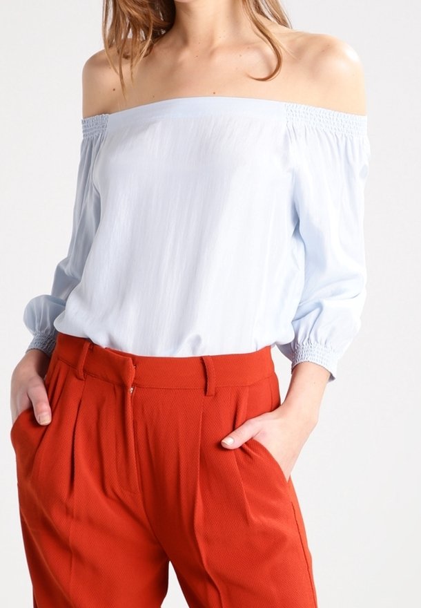 Blouse bleu clair à épaules dénudées avec poignets de manches froncés, associée à un pantalon orange texturé taille haute avec poches avant.