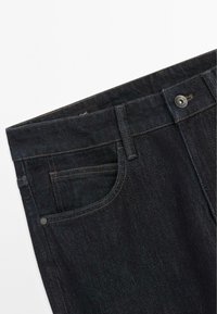 Dark blue denim jeans with a visible front pocket, gold stitching, and a metal button closure. The fabric has a subtle texture.