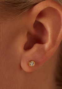 Créole en or avec une pierre précieuse ronde et transparente, centralement sertie dans un design lisse en sertissage, mettant en valeur une finition polie.