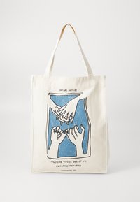 Canvas tote bag, cream color, features blue graphic of hands with text below. Sturdy handles for easy carrying. Simple, functional design.