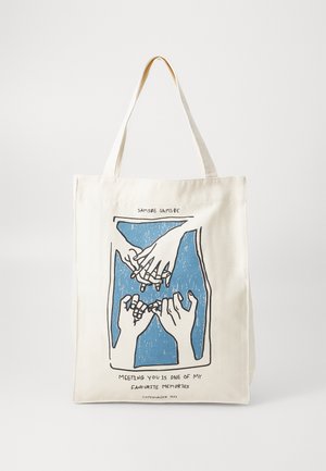 Canvas tote bag, cream color, features blue graphic of hands with text below. Sturdy handles for easy carrying. Simple, functional design.