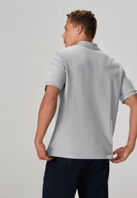 Graues Poloshirt mit kurzen Ärmeln, strukturierter Stoff, gerader Saum und Kragen. Kombiniert mit dunkelblauen Jeanshosen mit lockerem Schnitt.