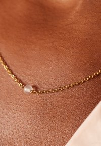 Gouden ketting met een ronde, matte kraal in het midden, rustend op een zachte huid, die het delicate en eenvoudige ontwerp benadrukt.
