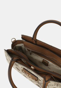 Sac à main beige et crème avec un extérieur texturé, double poignées et plusieurs compartiments intérieurs, comprenant une poche zippée et une doublure avec logo.
