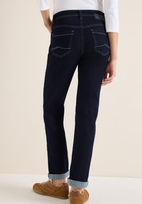 Jeans de denim azul oscuro con corte recto, con bajos enrollados, dos bolsillos traseros y detalles de costura blanca en contraste.