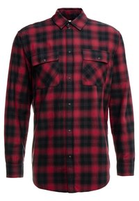 Röd och svart rutig skjorta i flanell med plaidmönster, långa ärmar, krage med knappar och två framfickor med tryckknappar.