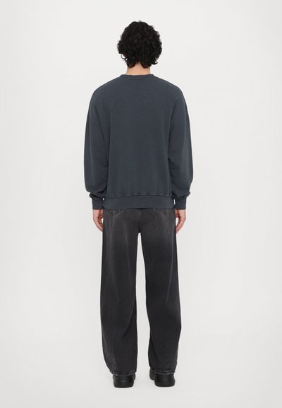 Sudadera de cuello redondo en gris oscuro con hombros caídos, combinada con jeans negros de corte holgado, vista desde la parte trasera. Textura suave.