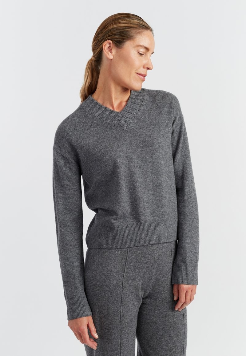 Grijze gebreide trui met een V-hals, geribbelde manchetten en zoom. Zachte textuur en een comfortabele pasvorm; gecombineerd met bijpassende grijze onderkleding.