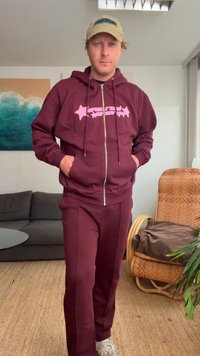 Felpa con zip color marrone e design grafico rosa, abbinata a pantaloni coordinati. Tessuto comodo, vestibilità rilassata e tasche laterali.