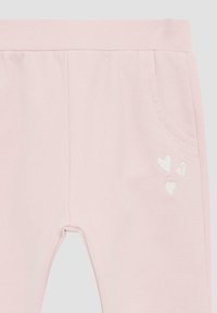 Helle rosa Baumwollhosen mit weicher Textur, einem Bund, Seitentaschen und einer kleinen weißen Herzstickerei auf der unteren linken Seite.