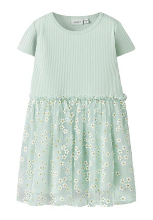 Vestito verde chiaro a maniche corte con top a coste e gonna trasparente decorato con motivi floreali di margherite bianche e gialle.