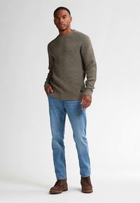 Donkergroene gebreide trui met een gestructureerd patroon, gecombineerd met lichtblauwe spijkerbroek en bruine laarzen, voorzien van een losse pasvorm en geribbelde manchetten.