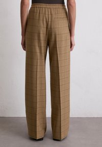 Braune Karohosen mit weitem Bein, elastischem Bund und einer einzelnen Gesäßtasche. Das Material wirkt strukturiert mit einem weichen Finish.