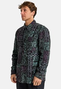 Camisa de franela a rayas en colores oscuros con diseños geométricos en azul petróleo y púrpura. Incluye un bolsillo con tapa abotonado y un cuello.
