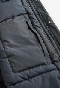 Padded jacket wykonany z ciemnoszarego materiału o gładkiej fakturze, z zapięciem na zamek oraz kieszenią zintegrowaną w designie.