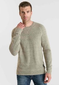 Hellgrauer, strukturierten Strickpullover mit langen Ärmeln, Rundhalsausschnitt und gerippten Bündchen, kombiniert mit blauen Jeans. Verfügt über ein kleines Etikett an der unteren Seite.