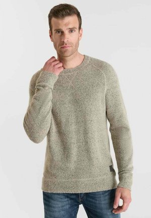 Lichtgrijze gestructureerde gebreide trui met lange mouwen, ronde hals en geribde manchetten, gedragen met blauwe jeans. Bevat een klein label aan de onderkant.